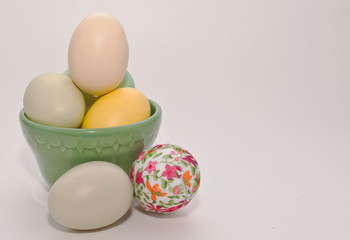 Six Easter eggs, four in a green cup and two laying in front of it on a white background. There is added room in the shot for text