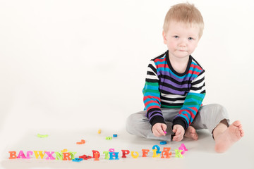 Happy charming Caucasian blond kid in colored clothes playing with plastic letters. Learning the alphabet, preparing for school. Education for kindergarten and preschool children. White background