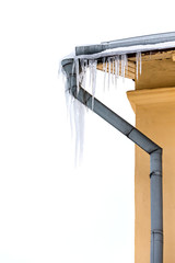 corner of house with drainpipe. icicles hanging down from the roof.