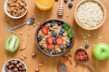 Healthy breakfast food on wooden table. Granola, oats, nuts, honey and fresh fruits. Table top view - obrazy, fototapety, plakaty