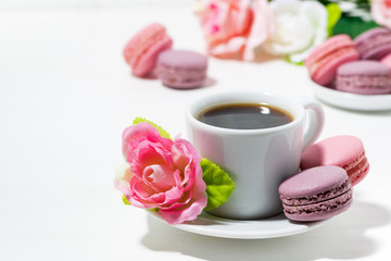 Fototapeta na wymiar macaroon cookies, cup of coffee and flowers on white table, closeup