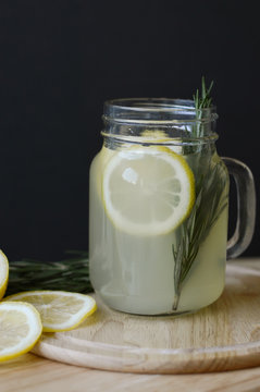 Lemonade with lemon slices and fresh rosemary leaves in glass jar on wooden board. Detox drink