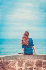 One girl with long blond hair sits by the sea. Toned image