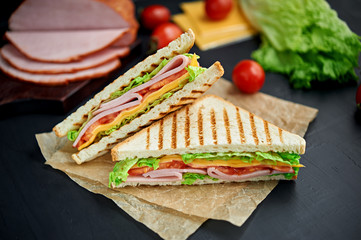 Sandwich with ham, cheese, tomatoes, lettuce, and toasted bread. Above view isolated on black background.