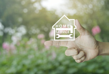 Hammer and wrench with house icon on finger over blur pink flower and tree, Home service concept