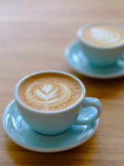 Two cup of coffee  in a beautiful blue cup on a wooden table in a coffee shop. A cappuccino mug with a pattern on the foam. 