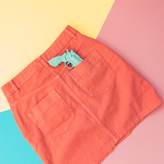 plastic gun in the pocket of the orange denim skirt. pastel minimal. fashion woman clothes
