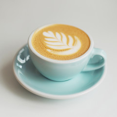A cup of coffee  in a beautiful blue cup on table in a coffee shop. A cappuccino mug with a pattern on the foam. 