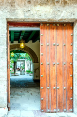 ancient wooden gate to the courtyard with an arch, palm trees, a well and a jug