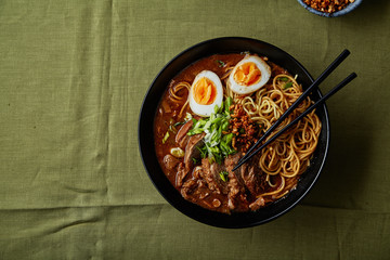 Japanese ramen with pork belly, mushrooms and marinated eggs on green linen tablecloth. Top view