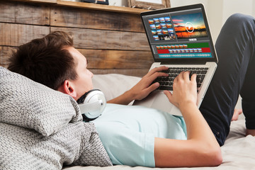 Man editing video with a laptop computer at home, while rest on the bed.