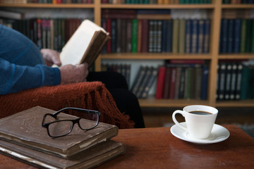 Sweet moments of relaxation with books and a cup of coffee. Vintage books, glasses, chair, library, man