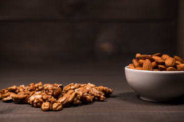 A white cup filled with almonds and scattered walnuts on a table
