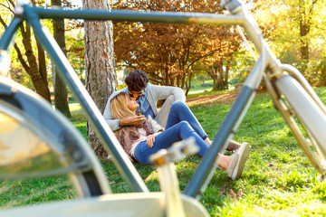 Young couple in love sitting in a autumn park leaning against a tree embracing one another.