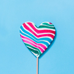 Lollipops rainbow colorful stripy candy as heart on blue. Funny concept. Top view. Square image.