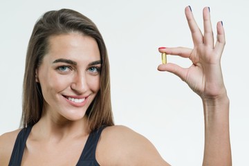 woman holds a capsule with vitamin E, fish oil. white background, focus on the capsule
