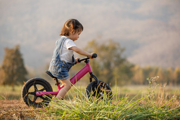 Happy child riding a bike. Little girl on a pink bicycle. Healthy preschool children summer activity. Kids playing outside. Little girl learns