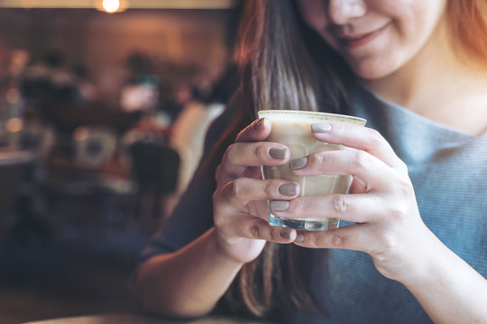 Closeup image of Asian woman holding and drinking hot coffee with feeling good in cafe