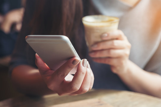 Closeup image of a woman's hand holding and using smartphone while drinking coffee in cafe