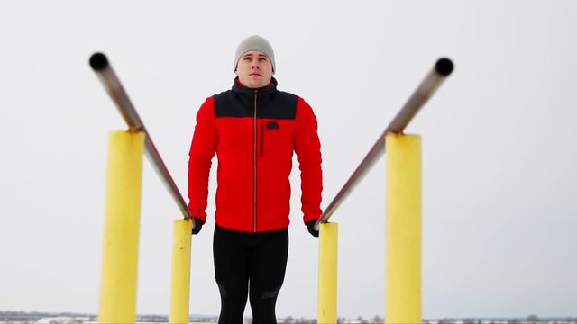 A sports trained man performs push-ups on parallel bars in the winter in the open air. Bottom view of the overall plan