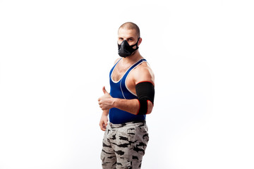 Young sportive man in blue tights,black elbow  and trainig mask stands and shows thumb up on a white isolated background