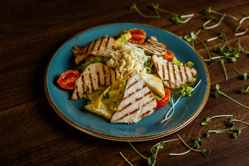 A horizontal image of a salad with grilled turkey, tomatoes, cheese, crusty white bread and mango mayonnaise, served on a blue plate, decorated with greenery. Selective focus.