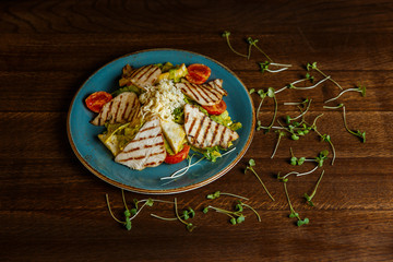 A horizontal image of a salad with grilled turkey, tomatoes, cheese, crusty white bread and mango mayonnaise, served on a blue plate, decorated with greenery. Selective focus.