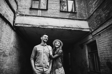 Black and white photo of a cheerful loving couple who stands against the background of the old building in stylish clothes and in a good mood. Love story