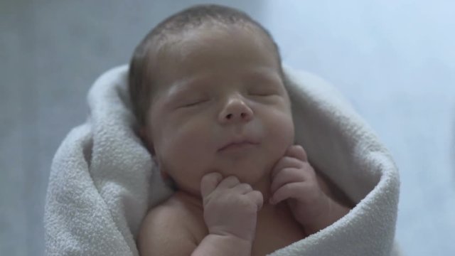 Adorable newborn baby sleeping in a blanket and holds his mother's hand
