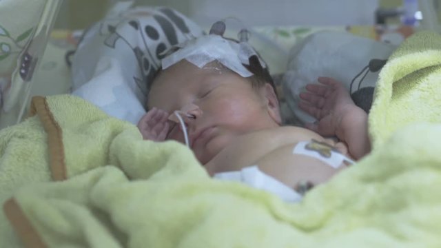 Newborn baby lying under blanket and sleeping in incubator
