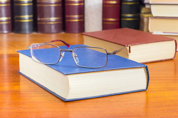 Eyeglasses on the closed book against of other books closeup