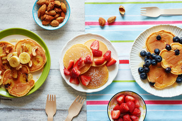 Homemade pancakes with strawberry, banana, blueberry, cashew, almond and honey on white table. Family breakfast for 3 person.