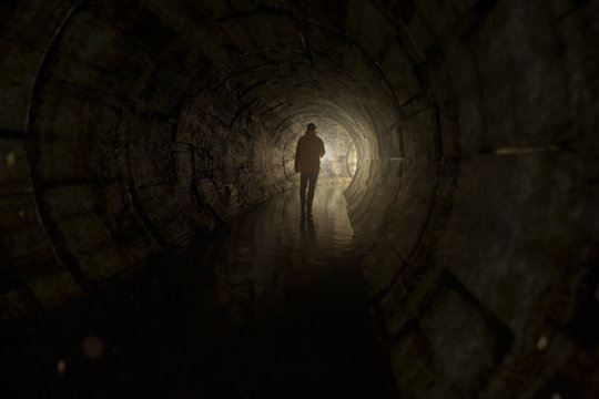 Mann läuft mit Taschenlampe durch Abwassertunnel