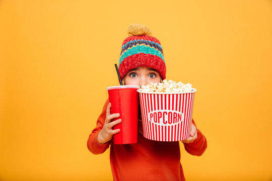 Scared Young girl in sweater and hat hiding behind popcorn