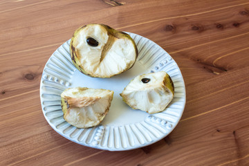 Centered white plate with one half and two quarters of a ripe cherimoya fruit Annona cherimola, central stem and seeds, horizontal aspect