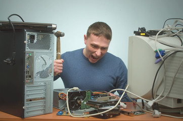 Enraged computer technician man is screaming and breaks a PC by hammer. PC repair service center. Mad system administrator in stress overburdened by work.