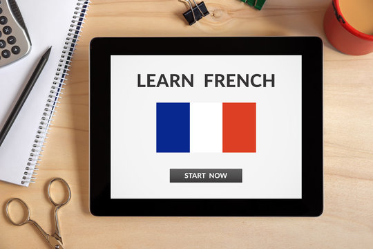 Learn French concept on tablet screen with office objects on wooden desk. All screen content is designed by me. Top view