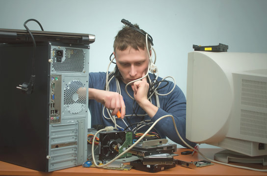 Tired and bored computer repairman is sitting on his workplace and thinking. Computer technician tired from his work and users. PC repair service center.
