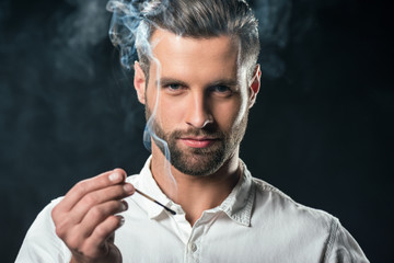 handsome businessman holding match with smoke, isolated on black