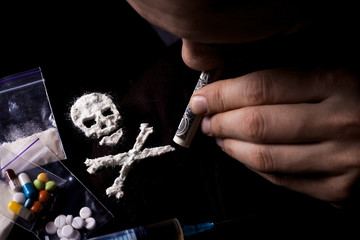 Drug dependence Kills. Junkie man sniffing a line of cocaine in the shape of a skull through a...