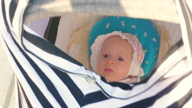 Baby girl in bonnet lying in pram during summer outing with mother