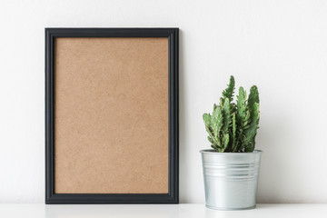 Modern room decoration. Cactus plant in white flower pot. Mock-up with a black frame.