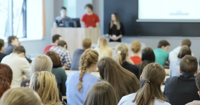 Group of university students sitting at their desks in auditorium and listening as their teacher holds a lecture.