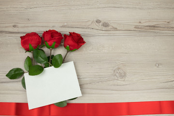 Red roses and a blank invitation card  on wooden background, decoration for Valentines Day, wedding day concept, copy space for text