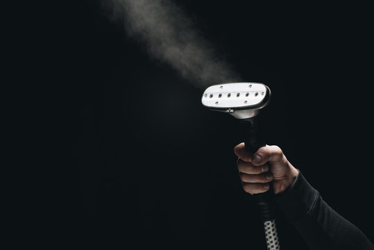 cropped shot of person holding garment steamer with steam on black