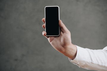 cropped shot of man holding smartphone with blank screen on grey