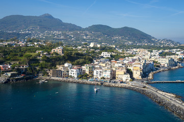 Fototapeta na wymiar Scenic overlook view of the waterfront village of Ischia Ponte with the volcanic mountains towering above the horizon on the Mediterranean island of Ischia, Italy