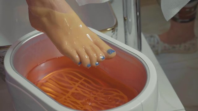 Wax bath for feet at beauty spa salon. Close-up in slow motion.