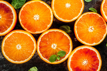 Fresh raw blood oranges, halves, with mint, on dark rusty background copy space top view