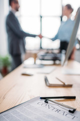 close-up shot of business contract lying on table and blurred business partners shaking hands on...
